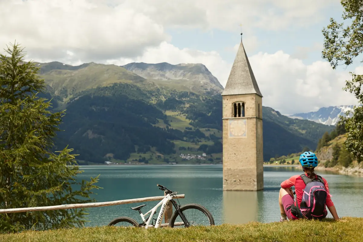 Mountainbikerin mit Blick auf den Kirchturm im Reschensee